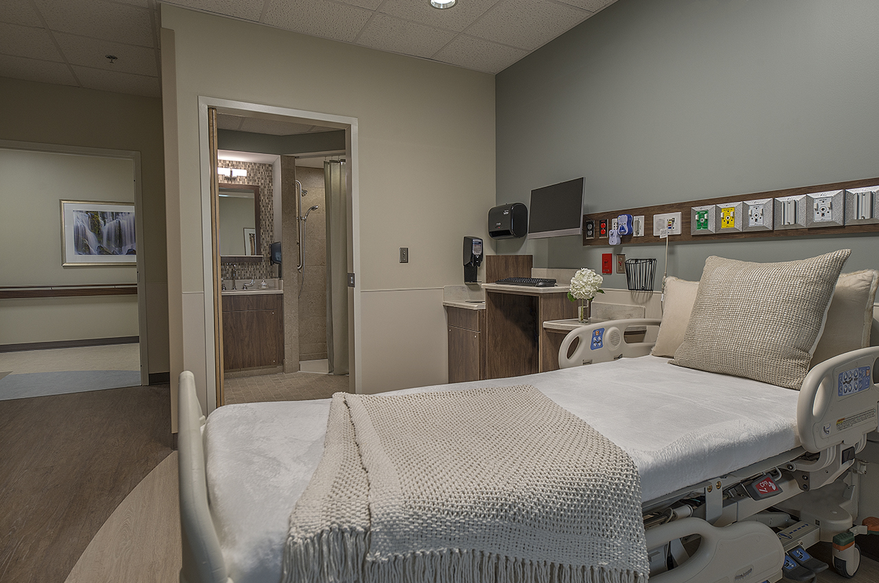 state-of-the-art patient room with calming color palette and view into bathroom with decorative mosaic tile, vanity, walk-in shower
